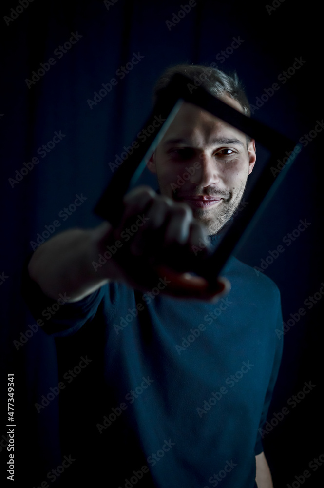 portrait of a young man holding a frame in front of his face, concept for the uniqueness of individuals portrait of a young man holding a frame in front of his face, concept for the uniqueness of individuals