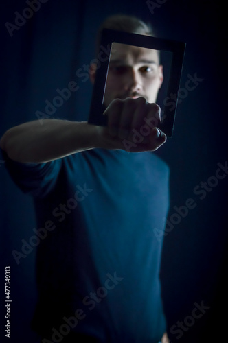portrait of a young man holding a frame in front of his face, concept for the uniqueness of individuals, focus on the hand  © sebastianosecondi