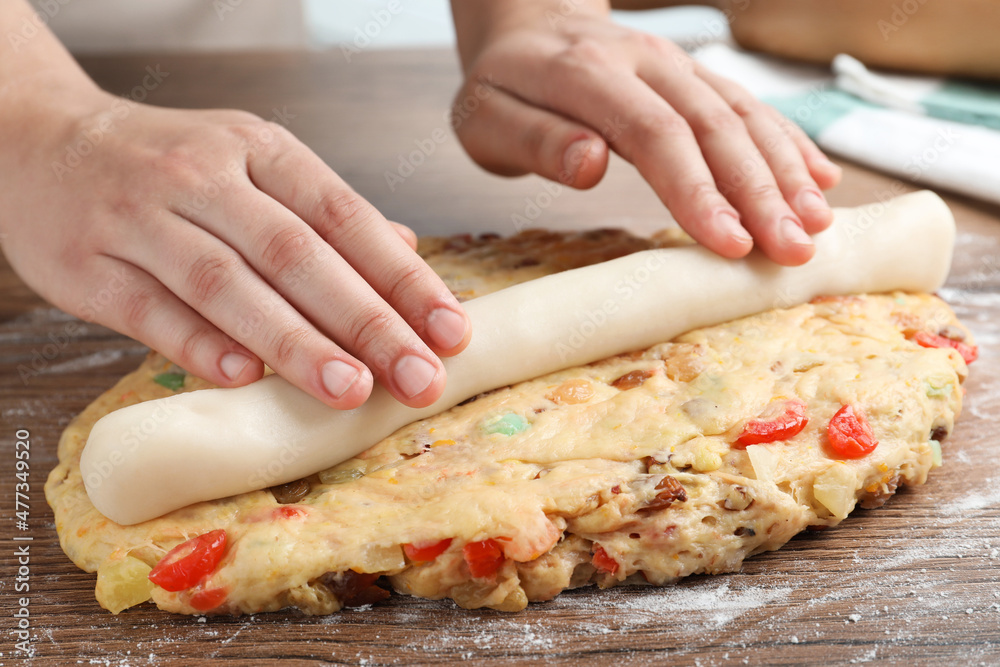 Woman putting marzipan into raw dough for Stollen at wooden table, closeup. Baking traditional German Christmas bread Woman putting marzipan into raw dough for Stollen at wooden table, closeup. Baking traditional German Christmas bread