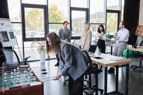 business people talking during coffee break in modern office near blurred woman playing table football.