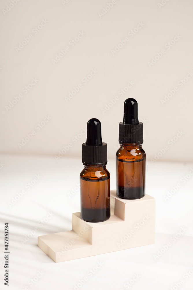 Amber glass bottles with dropper pipette with serum or essential oil on concrete plate for product presentation with palm leaves shadow. Skin care cosmetic. Beauty concept for face body care
