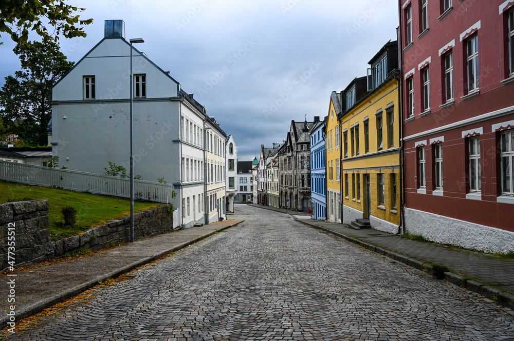 Empty street with colorful houses in the city of Alesund, Norway. Leaves of a tree are framing the picture. No people are on the road due to the Corona pandemic. 