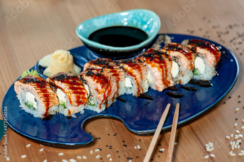 sushi roll dragon with eel on a blue plate with sauce sticks and ginger
