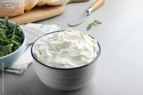 Bowl of tasty cream cheese on grey table