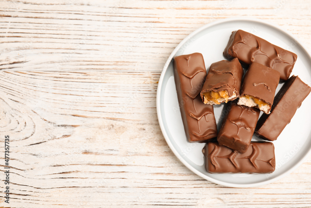 Plate of chocolate bars with caramel, nuts and nougat on white wooden table, top view. Space for text Plate of chocolate bars with caramel, nuts and nougat on white wooden table, top view. Space for text