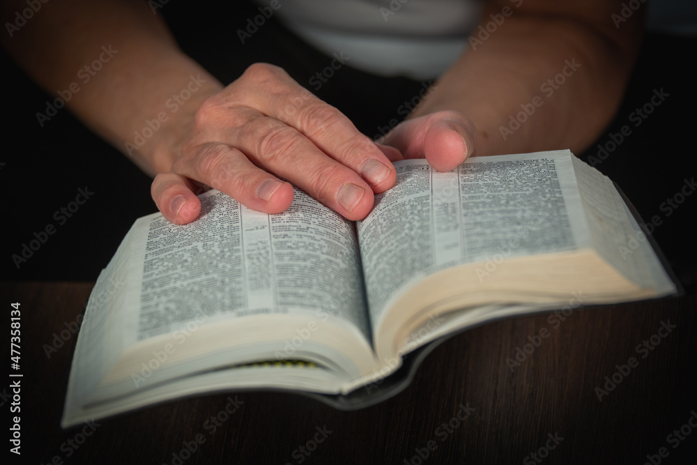 An older woman (old woman) reads a book, the Bible in transliteration in Russian. An elderly lady and her hands. An older woman (old woman) reads a book, the Bible in transliteration in Russian. An elderly lady and her hands.