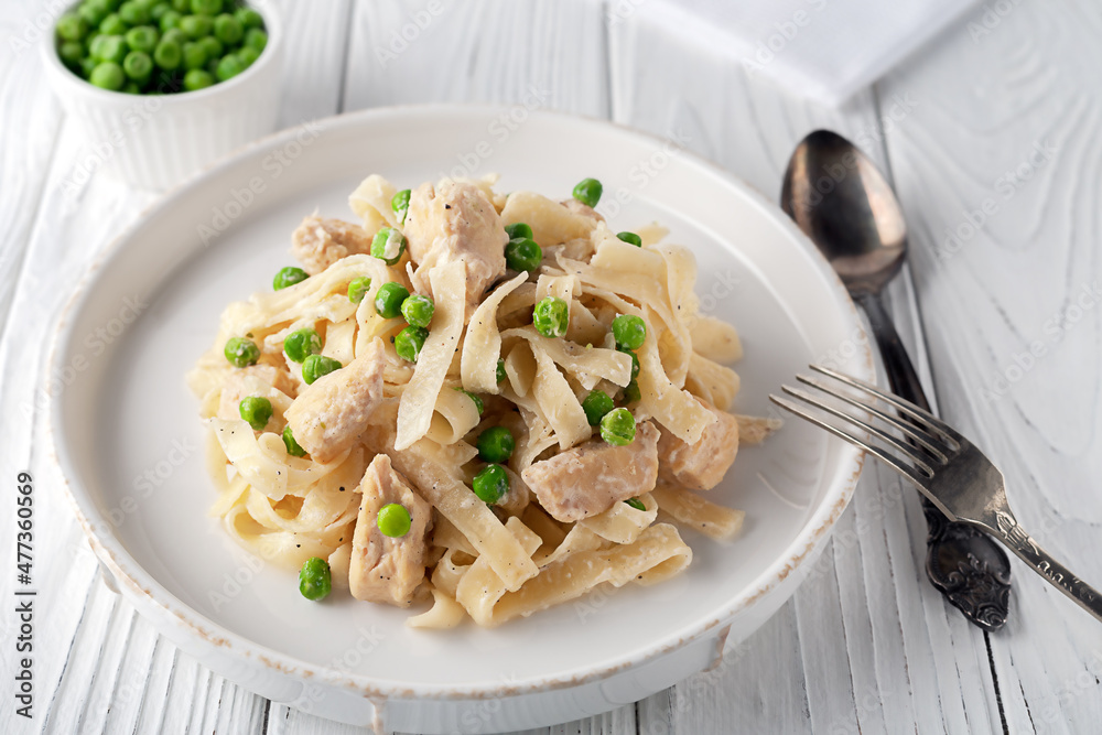 Homemade pasta with green peas, chicken and cream sauce on a white wooden background on a white wooden background