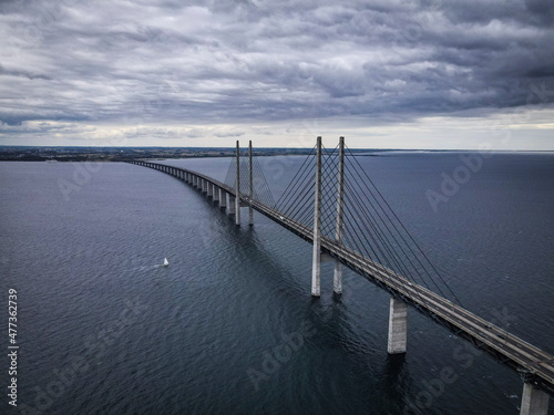 Aerial view of sailboat sailing under Oresund bridge, on a dramatic windy and cloudy day, Denmark. photo