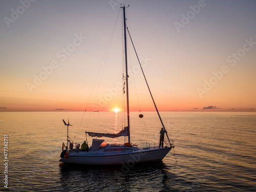 Aerial view of sailboat mooring in the sea and two sailors watching sunrise near Mons Klint, Denmark. photo
