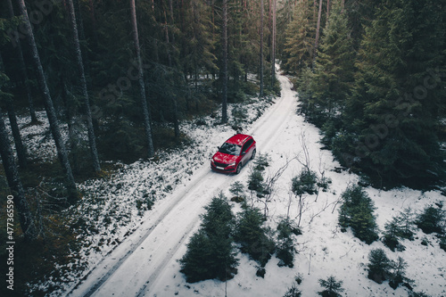 Aerial view of red car on a winding snowy forest road in winter, Korvemaa, Harjumaa, Estonia. photo