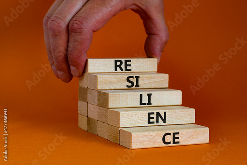 Resilience symbol. Wooden blocks with the word Resilience. Beautiful orange background, copy space. Businessman hand. Business, resilience concept.