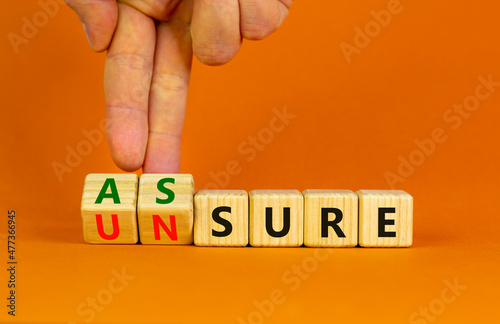 Assure or unsure symbol. Businessman turns wooden cubes and changes the concept word unsure to assure. Beautiful orange table, orange background, copy space. Business and assure or unsure concept. photo