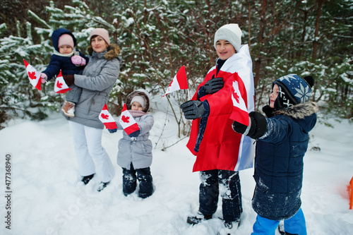Mother with kids holding flag of Canada on winter landscape.