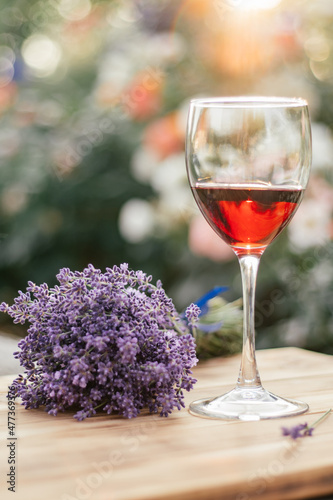 half-empty glass of red wine and lavender bouquet tied with blue ribbon on wooden brown table in sunny day at sunset in garden against organic background. soft focus. vertical