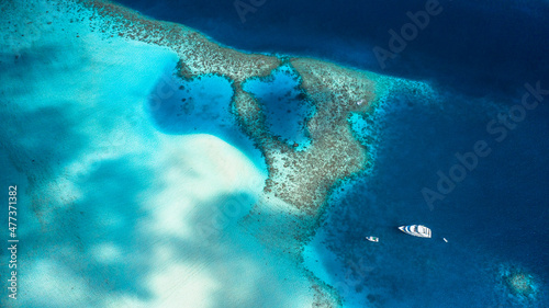 Panoramic aerial view of a sandbank with shadows of clouds and an anchored yacht, Maldives.