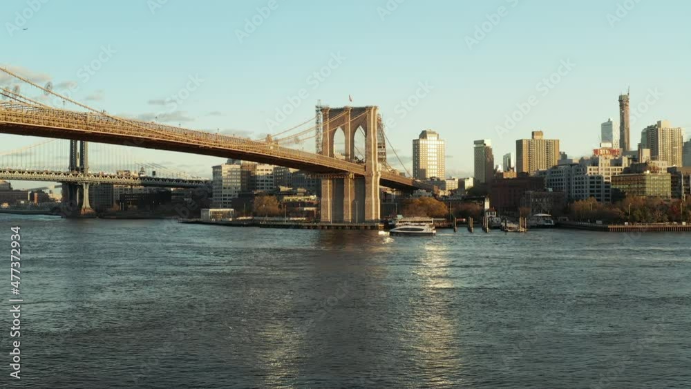 Low flight above water, cruise ship floating on surface under Brooklyn Bridge. High rise buildings in background. Brooklyn, New York City, USA Low flight above water, cruise ship floating on surface under Brooklyn Bridge. High rise buildings in background. Brooklyn, New York City, USA