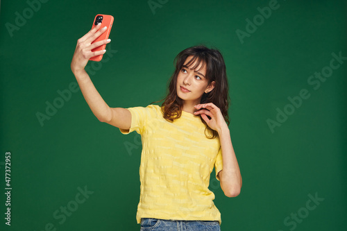 Modern young girl beauty blogger make selfie on phone, shoot photo for social network content posing on green background © Georgii