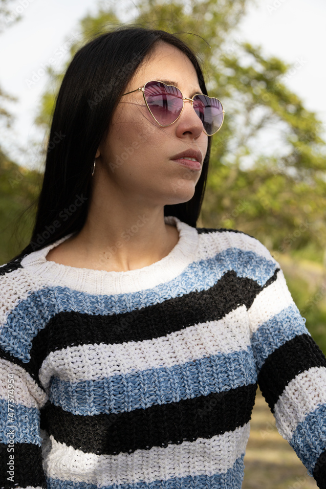 detail of the face of a young latin woman with straight black hair, wears fashionable sunglasses in the shape of a heart as an accessory, natural beauty of a model in a park detail of the face of a young latin woman with straight black hair, wears fashionable sunglasses in the shape of a heart as an accessory, natural beauty of a model in a park