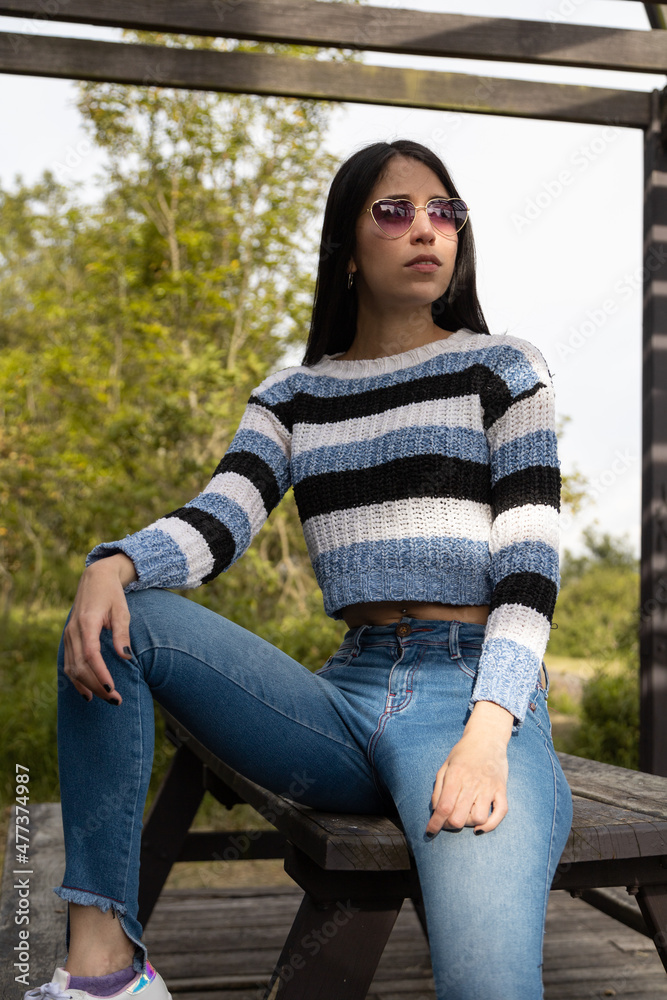 full body of young latin woman with straight black hair sitting relaxed on a park bench, wearing sunglasses and casual clothes, beauty and fashion full body of young latin woman with straight black hair sitting relaxed on a park bench, wearing sunglasses and casual clothes, beauty and fashion