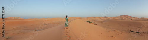 Panoramic picture of Yellow  golden and arid desert view. Camel in hot Sahara. Caucasian Woman with green dress.