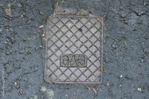 Gas manhole cover. Square metal cover with square texture with gas written on it. Brown metal within black pavement.