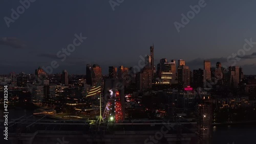 Forwards fly above American flag on top of Brooklyn Bridge. Heavy traffic in evening city. Panoramic view of high rise buildings at dusk. Brooklyn, New York City, USA