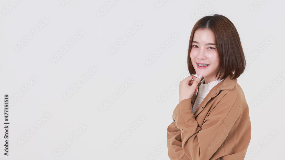 Portrait closeup studio cutout shot of Asian young beautiful short hair female model in brown coat jacket standing smiling look at camera pointing finger up on blank copy space on white background Portrait closeup studio cutout shot of Asian young beautiful short hair female model in brown coat jacket standing smiling look at camera pointing finger up on blank copy space on white background