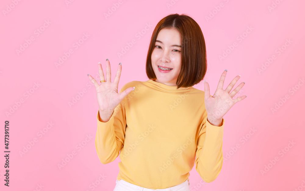 Portrait studio cutout shot of Asian young pretty short hair female model in yellow long sleeve shirt stand smile to look at the camera and pointing finger on pink background. Portrait studio cutout shot of Asian young pretty short hair female model in yellow long sleeve shirt stand smile to look at the camera and pointing finger on pink background.