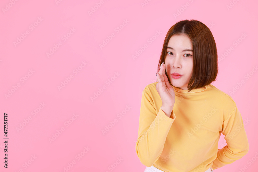 Portrait studio cutout shot of Asian young pretty short hair female model in yellow long sleeve shirt stand smile to look at the camera and pointing finger on pink background. Portrait studio cutout shot of Asian young pretty short hair female model in yellow long sleeve shirt stand smile to look at the camera and pointing finger on pink background.