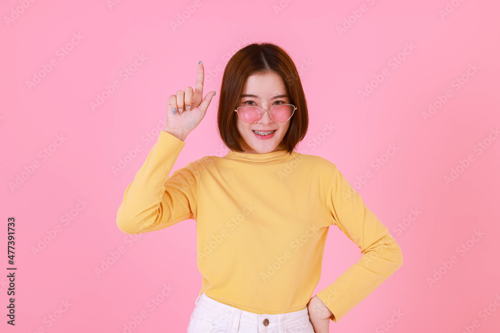 Portrait studio cutout shot Asian young pretty short hair female stylish fashionable model in yellow long sleeve shirt standing look at camera holding adjusting fashion sunglasses on pink background Portrait studio cutout shot Asian young pretty short hair female stylish fashionable model in yellow long sleeve shirt standing look at camera holding adjusting fashion sunglasses on pink background