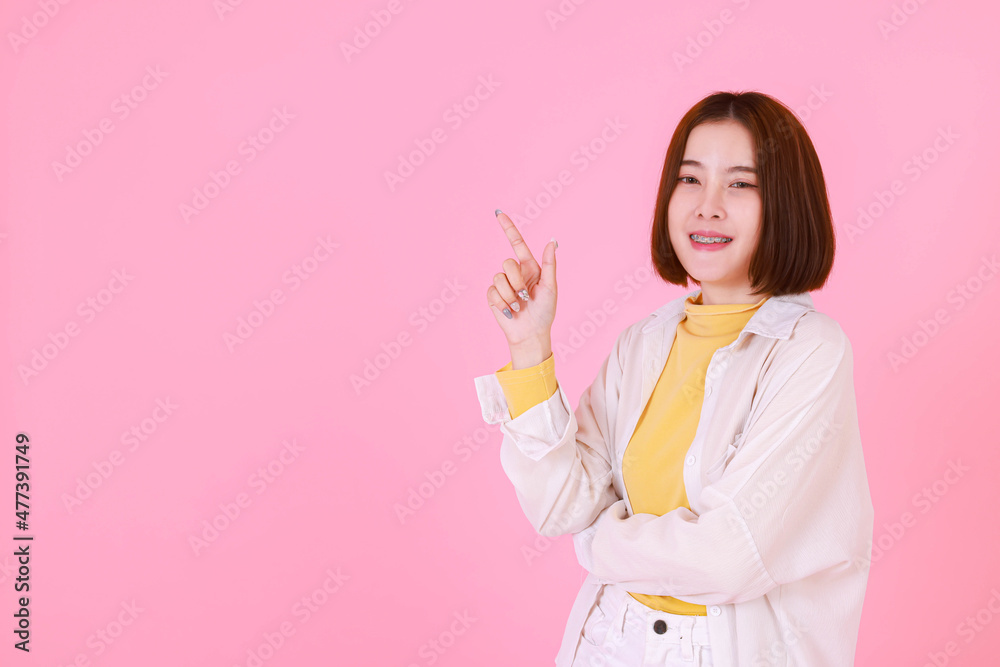 Portrait studio cutout shot Asian young pretty short hair female stylish model in yellow long sleeve shirt and jacket stand smile look at camera hold hand point up blank copy space on pink background Portrait studio cutout shot Asian young pretty short hair female stylish model in yellow long sleeve shirt and jacket stand smile look at camera hold hand point up blank copy space on pink background