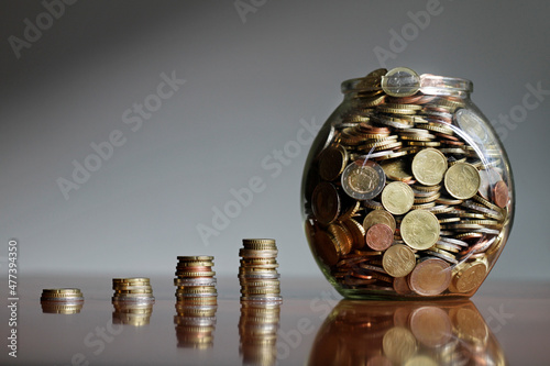 Growing stacks of Euro coins and a clear glass jar with money photo