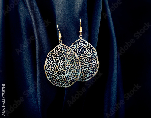 Round metal earrings hanging on blue silk background.