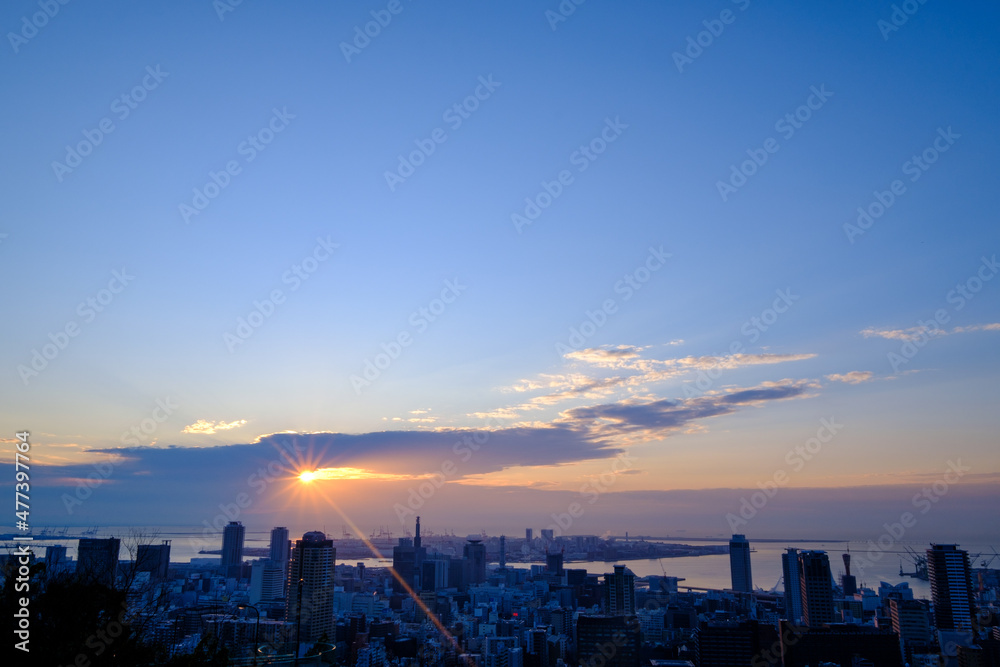 都市の夜明け。日の出の時間が過ぎるが、太陽は厚い雲に隠れていたが、ようやく雲の切れ目から顔を出す。神戸の山手ヴィーナスブリッジから撮影