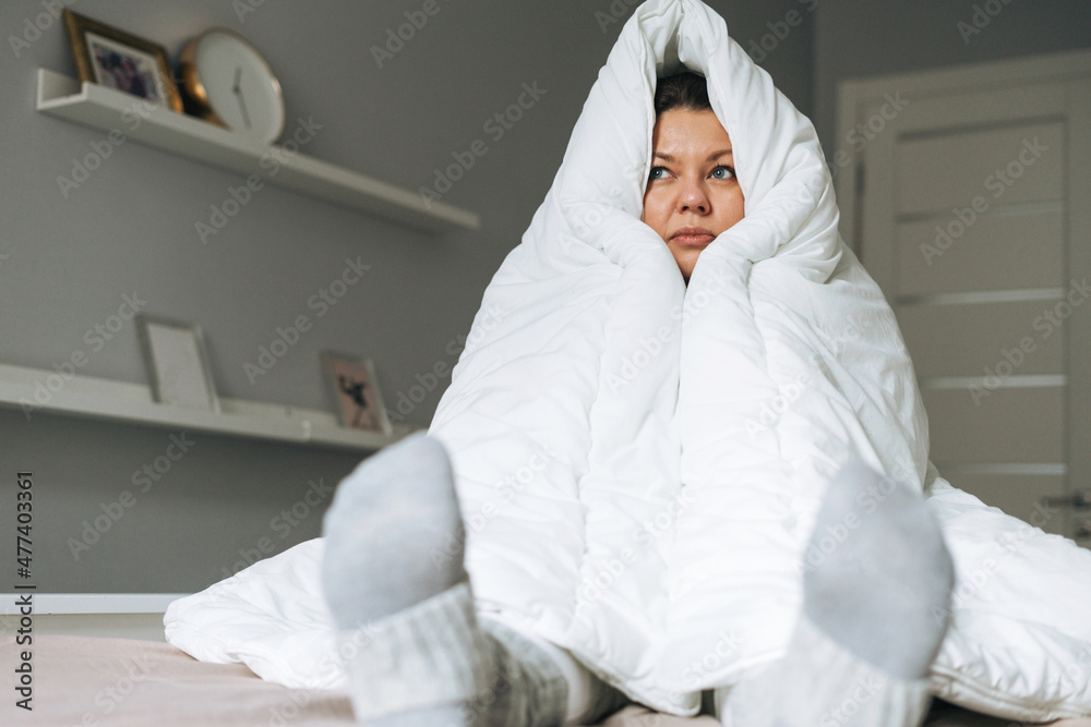 Young adult unhappy lonely woman forty years plus size body positive in white big blanket on bed at the home Young adult unhappy lonely woman forty years plus size body positive in white big blanket on bed at the home