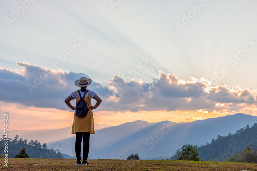 Travel young girl with backpack and hat enjoying sunset on peak mountain. Tourist traveler on background valley landscape view mockup. Rear view © AungMyo