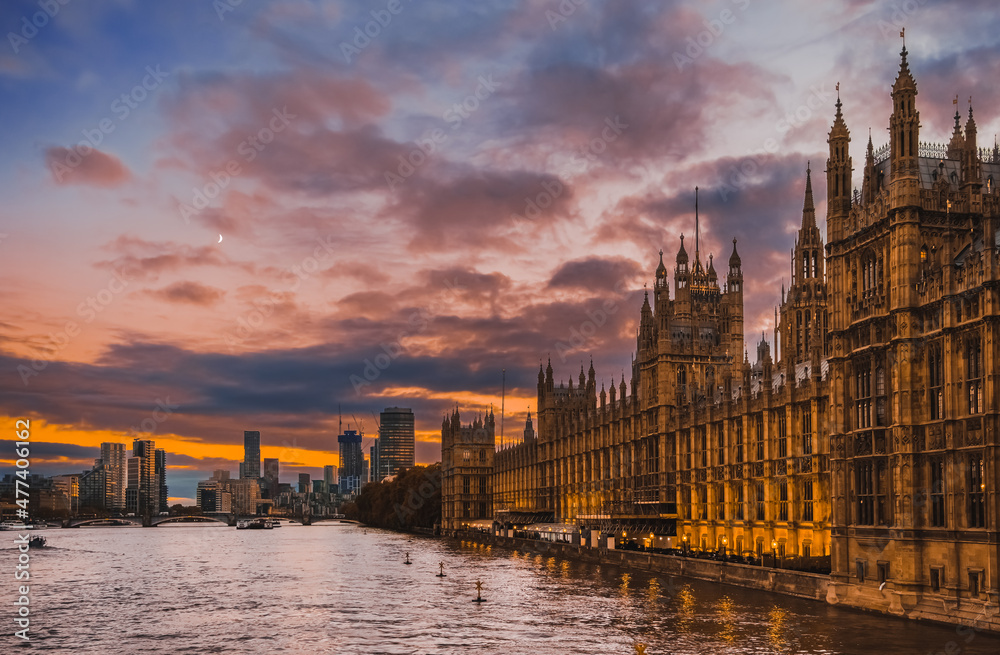 Beautiful view of Parliament buildings, Big Ben, and other buildings of City of Westminster at sunset , in London, England; buildings and clouds reflect in River Thames