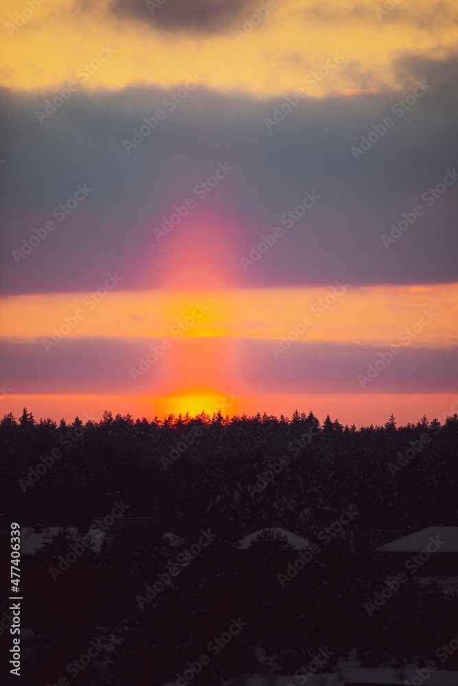 Obraz premium Bright orange sunset pillar in the sky. Rare optical phenomenon in winter, illuminated ice crystals in the air. Selective focus on the details, blurred background.