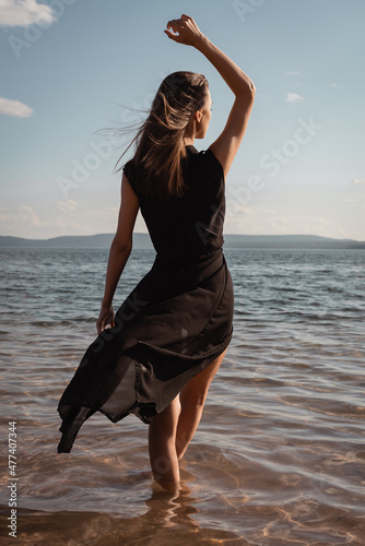 A young woman in a black dress stands in the water by the sea. High quality photo