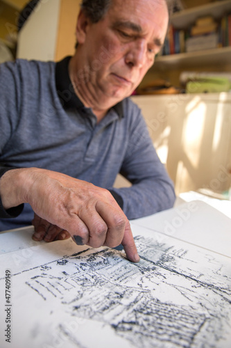 Close up of a focused senior man drawing a pastel sketch sitting at table indoors, vertical frame.