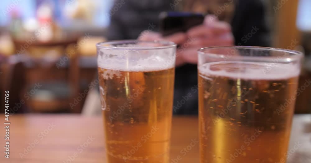 Close up view of 2 glasses of draft beer (draught beer) on a table with a blurred pub in the background. 4K video. Close up view of 2 glasses of draft beer (draught beer) on a table with a blurred pub in the background. 4K video.