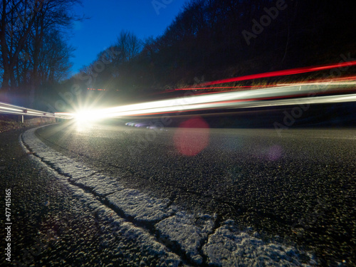 Trazas de luz dejadas por un vehículo al tomar una curva por la noche en una carretera de montaña. El primer plano es ocupado por la línea lateral de la calzada. photo