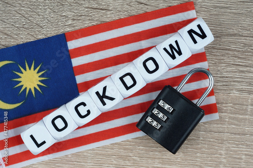 LOCKDOWN wording on a blocks with a black padlocks a over a wooden background an Malaysia flag. Lockdown during pandemic