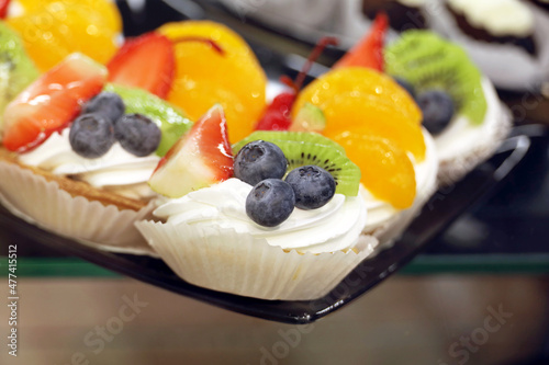 Creamy cakes with fresh fruits and berries, selective focus. Sweet cream dessert with blueberries, tangerines, kiwi and strawberry