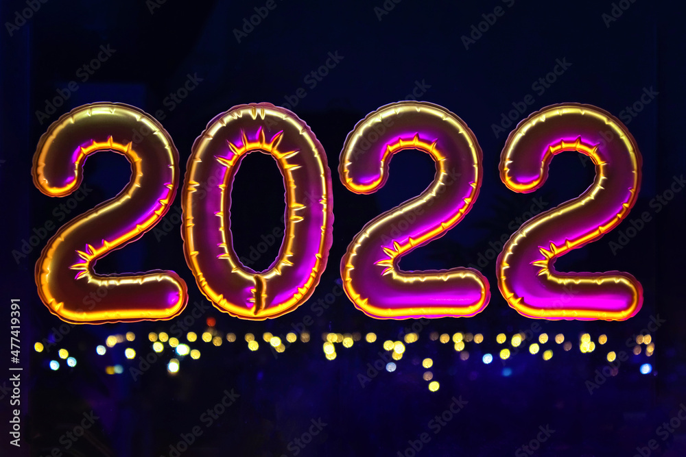 Gold inflatable foil balloons numbers 2022 on the window against the background of the night city, in neon light. New year 2022, christmas. Gold inflatable foil balloons numbers 2022 on the window against the background of the night city, in neon light. New year 2022, christmas.