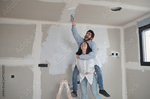 Fotografie Woman give her friend a piggyback ride to paint the ceiling in their new house