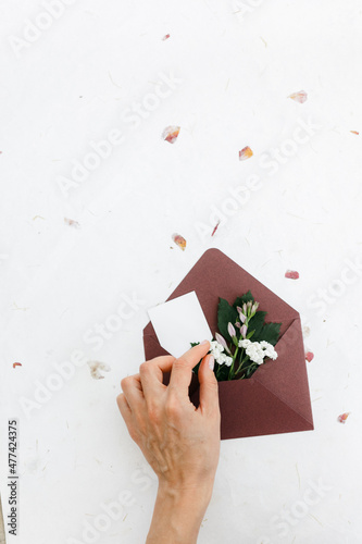 Bard cardboard envelope top view. fresh flowers and a postcard are inserted into the envelope. Female hands adjust the envelope. space for text.