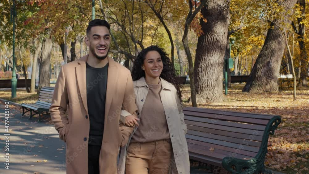 Young family walking in autumn park enjoying pleasant conversations on romantic date girl holding guy hand happy couple spend carefree weekend together outdoors hispanic man and woman joyfully smiling Young family walking in autumn park enjoying pleasant conversations on romantic date girl holding guy hand happy couple spend carefree weekend together outdoors hispanic man and woman joyfully smiling