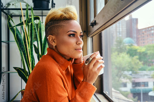 Photography Portrait of a young woman looking out urban window having coffee at home