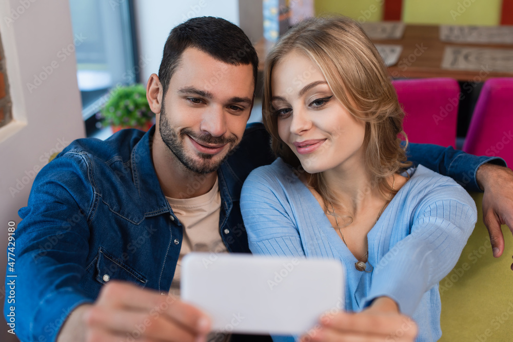 pleased couple taking selfie on blurred cellphone while spending time in cafe pleased couple taking selfie on blurred cellphone while spending time in cafe